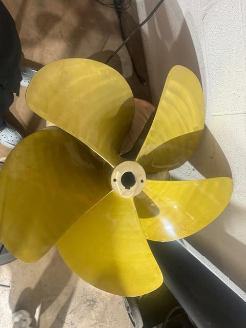 Yellow propeller with four curved blades and white center hub lying on cardboard