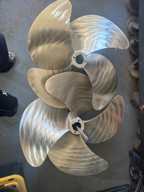 Two bronze boat propellers with curved blades displayed on a concrete floor in a workshop setting