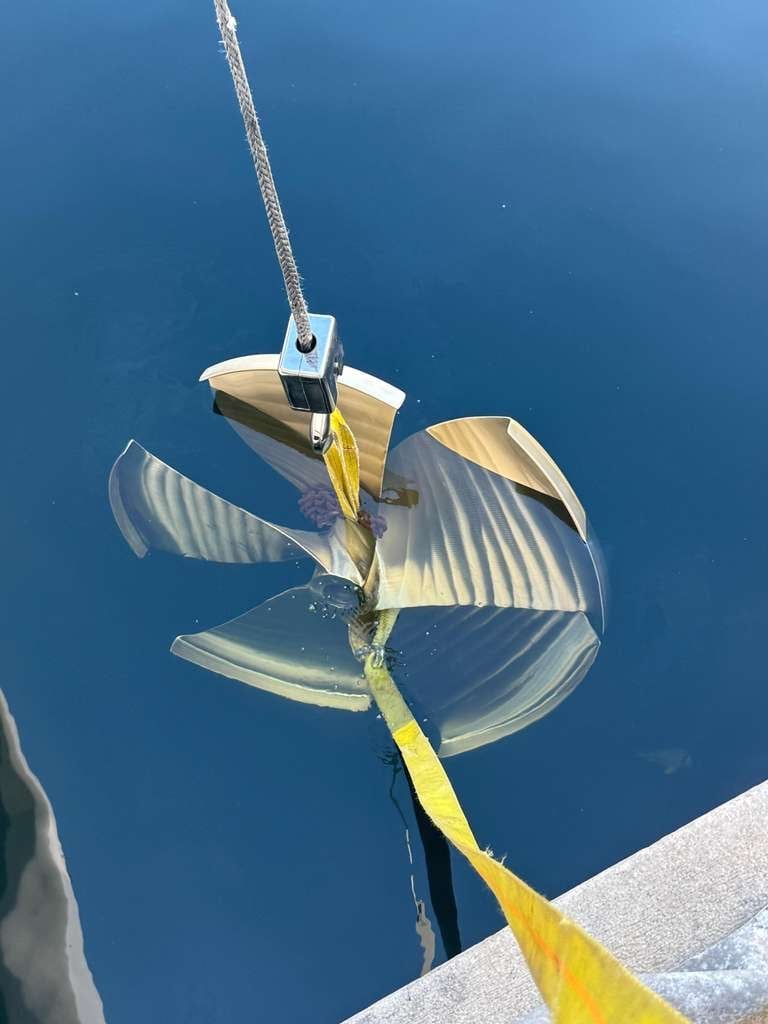 Folded boat anchor with yellow rope and metal bridle submerged in blue ocean water
