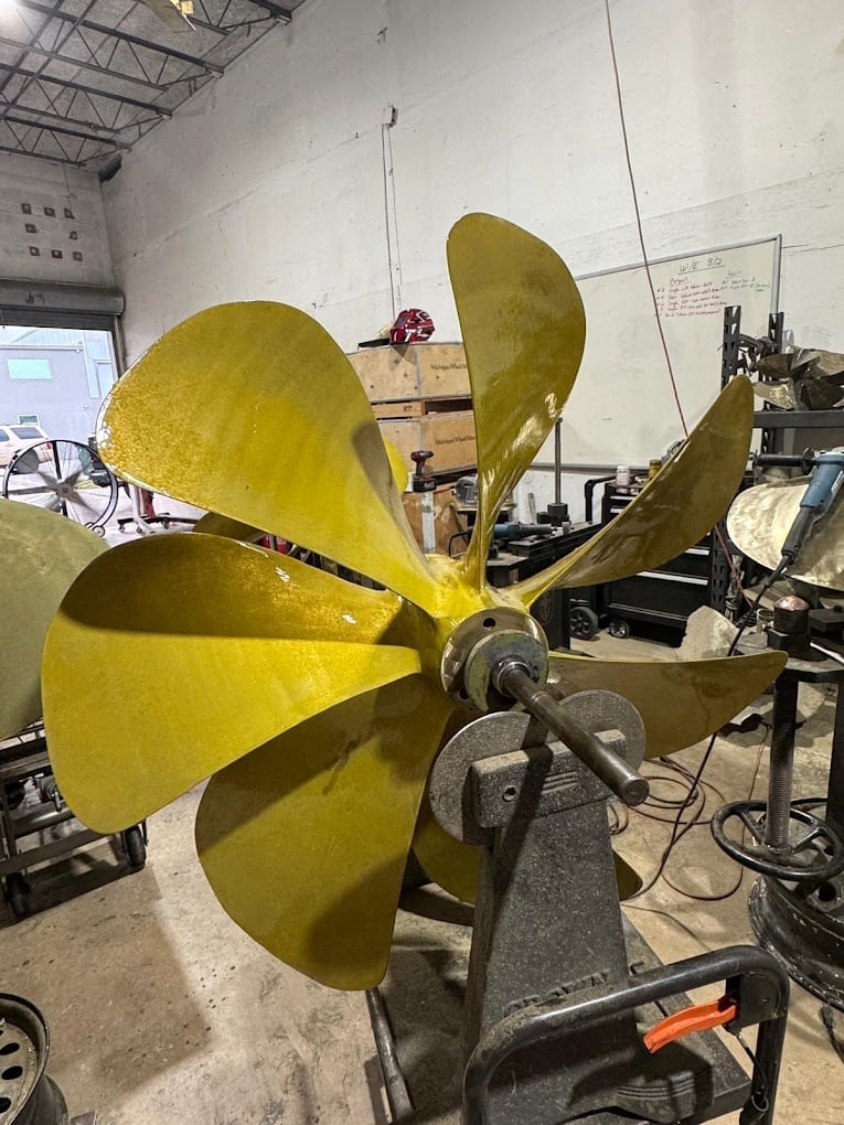 Large yellow propeller mounted on equipment in an industrial workshop setting