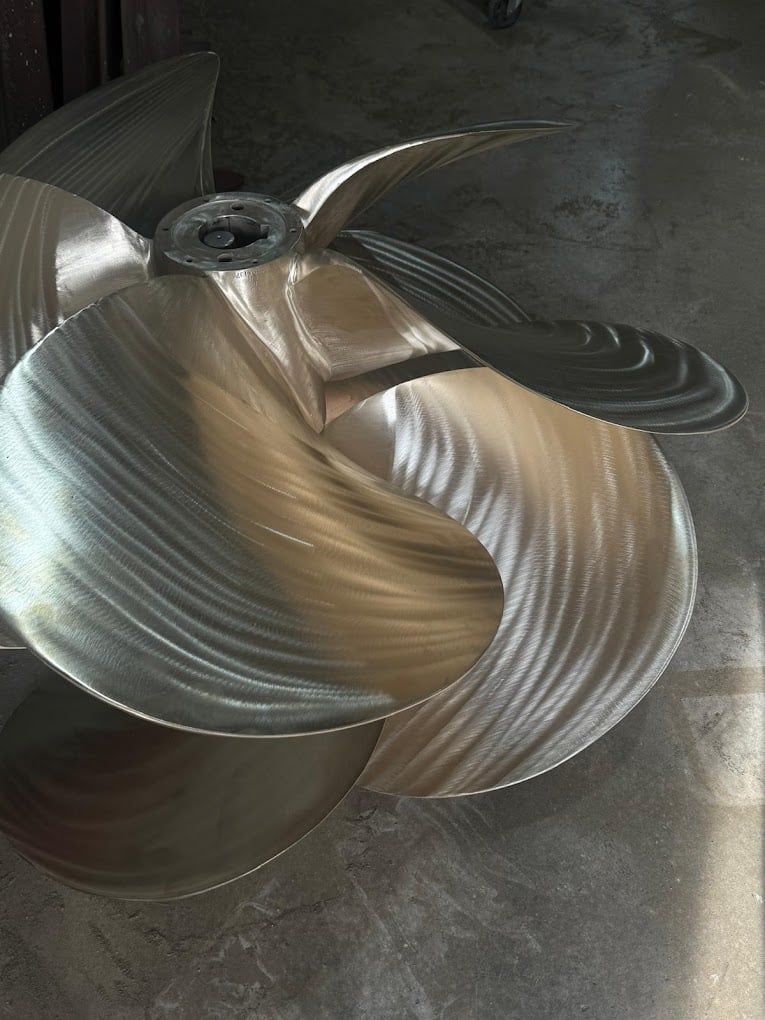 Large metal industrial fan blade parts with curved ribbed sections lying on concrete floor
