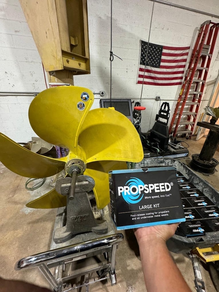 Person holding PropSpeed large kit box next to yellow boat propeller in workshop with American flag and tools