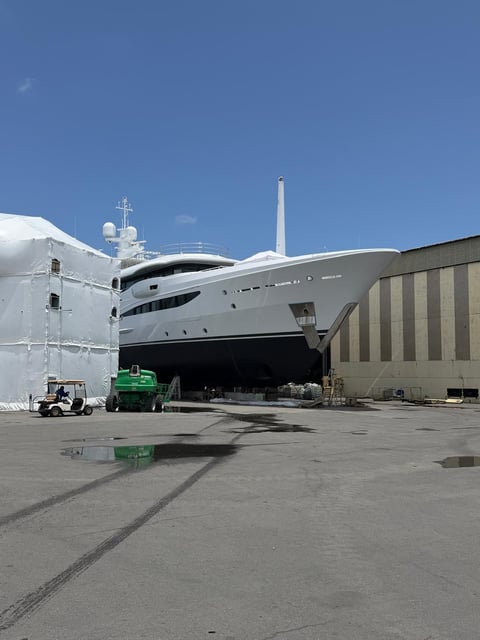 Large luxury yacht in dry dock at a shipyard with maintenance equipment and industrial building, clear blue sky