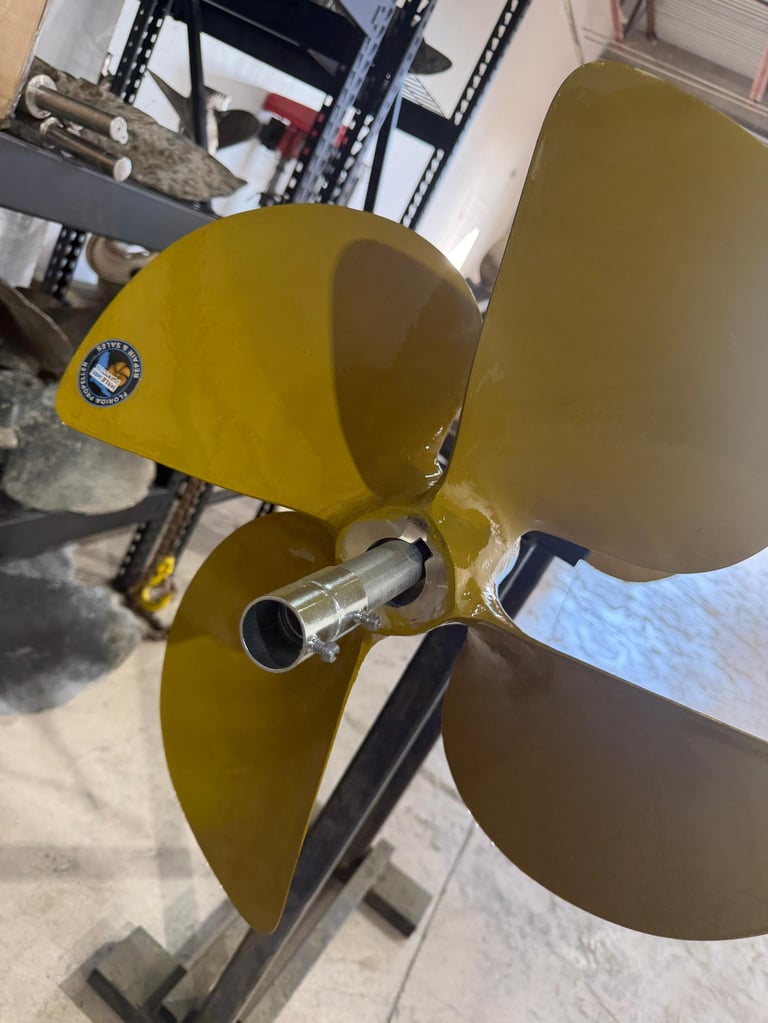 Close-up of a yellow and brown three-blade marine propeller with a center hub and shaft in an indoor workshop setting