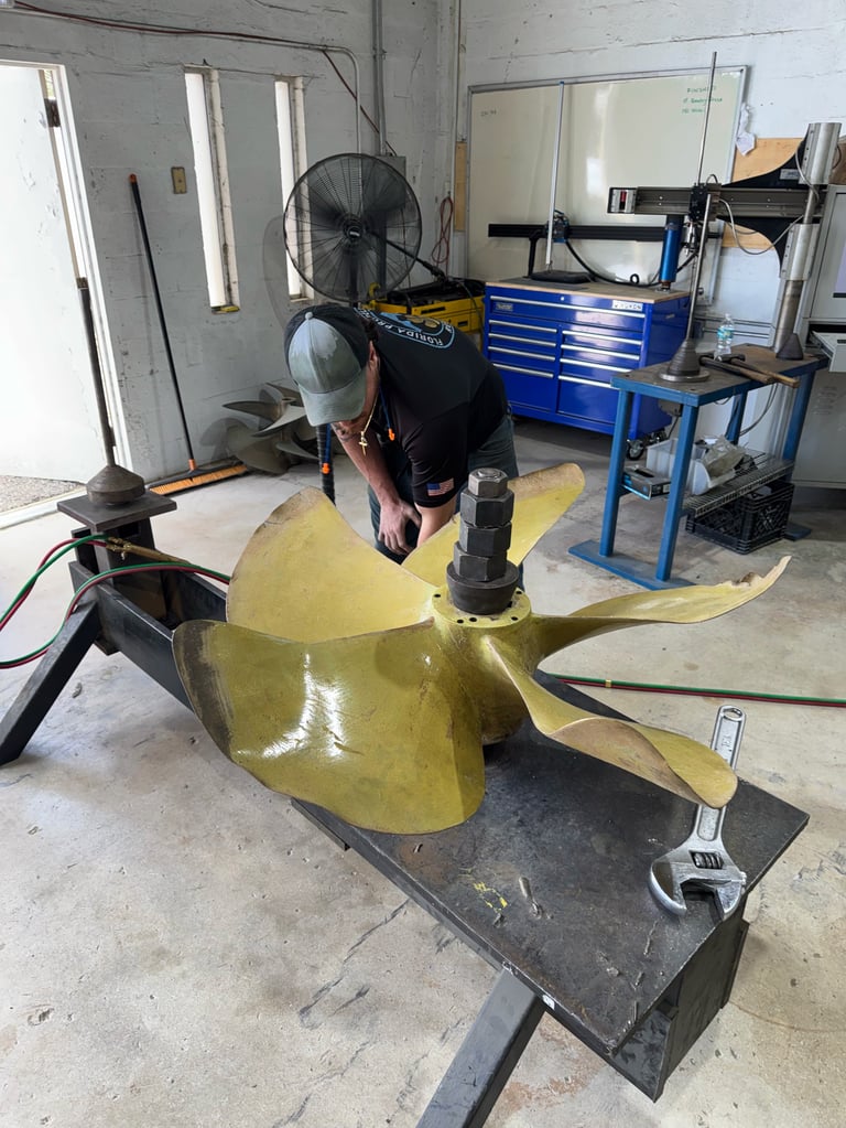 Worker in protective gear applying yellow coating to large industrial part in workshop with blue tool storage and ventilation fans