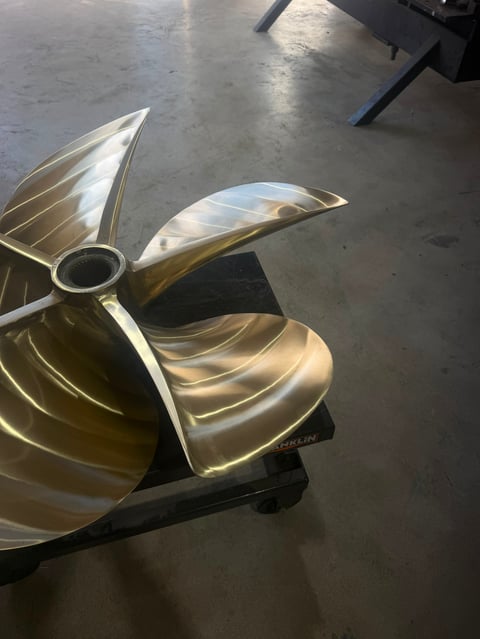 Large brass three-bladed ship propeller mounted on concrete floor in industrial setting