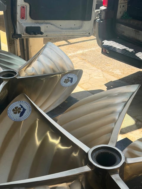 Two large metallic boat propellers with white trim displayed on sandy ground next to vehicles